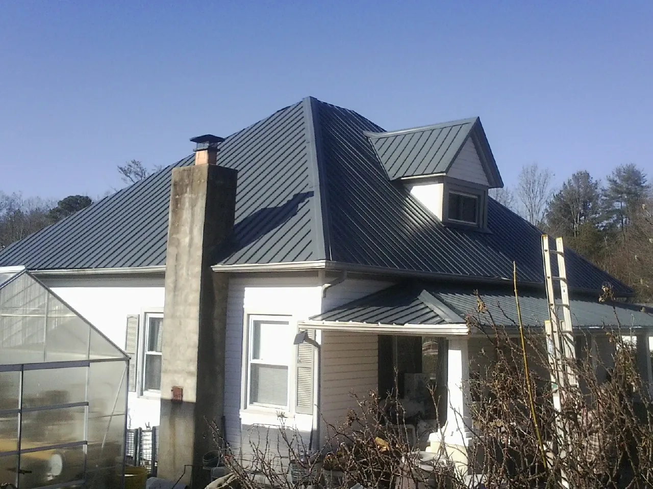 Dark blue standing seam metal roof on a white farmhouse with dormer — Slate & Tile Roof Repair by Roofing Brothers in Mapleton