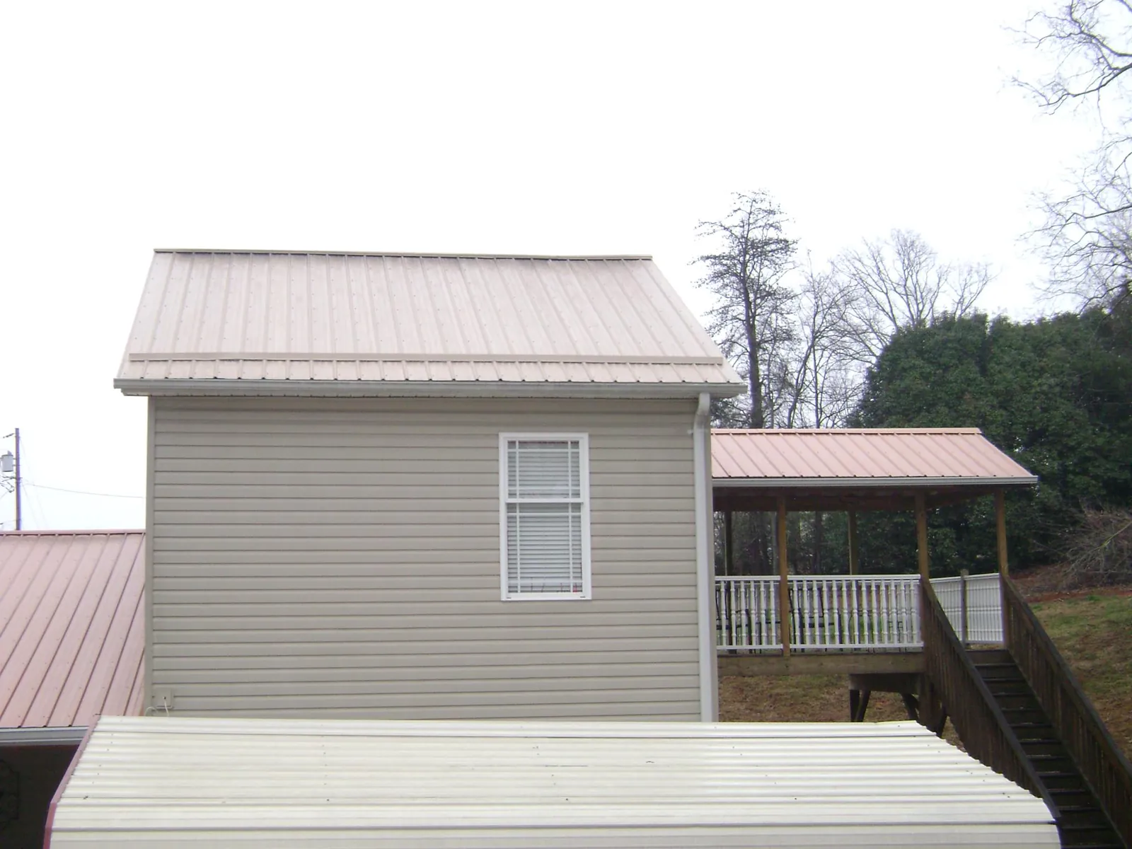Tan metal roofs on a two story addition and attached porch, from a Roof Replacement job in Mapleton